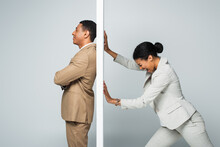 Angry African American Businesswoman Screaming And Pulling Wall Near Smiling Businessman On Grey