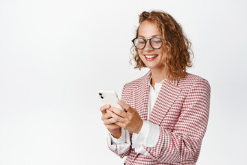 Cellular technology. Smiling business woman in glasses chatting, using mobile phone, reading smartphone, standing over white background