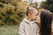 © Ananass - Young happy and smiling mom with her little daughter in arms hugging and kissing spending a weekend on a walk in autumn park. selective focus, noise effect, Autumnal mood