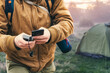 Man holds a smartphone in his hands and charges it with a power bank against the backdrop of a tourist tent in nature. Portable travel charger.