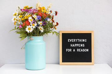 Wall Mural - Everything happens for a reason. Motivational quote on letter board and bouquet colorful flowers on white table against grey stone wall. Concept inspirational quote of the day
