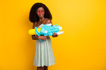 Poster - Photo of young afro girl hold water gun toy play game shoot summer pool party isolated over yellow color background