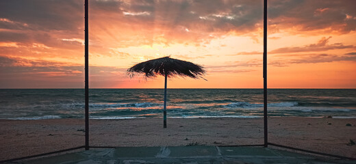 Wall Mural - Beach umbrella on the shore of the summer sea during sunrise. Horizontal banner, the concept of summer holiday