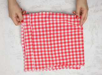 Wall Mural - two female hands hold a crumpled white-red checkered textile kitchen napkin on a white table