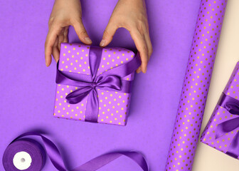 Wall Mural - two female hands are holding purple gift box on paper background, concept of congratulations on birthday