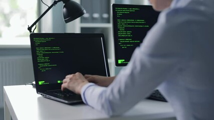 Back view of female programist using two modern computers for doing code programming at office. Software developer working on modern gadgets at IT center.