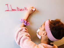 Young Girl Wearing A Mask Writing On A Whiteboard