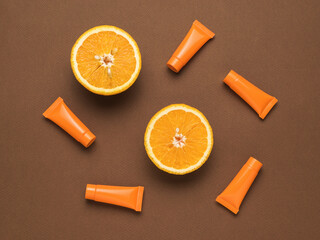 Two halves of an orange and five tubes of cream on a brown background. Flat lay.