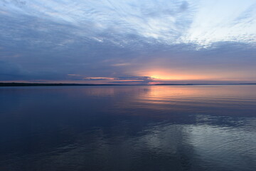 Wall Mural - Sunset glow in the clouds on the horizon on the horizon over  calm water