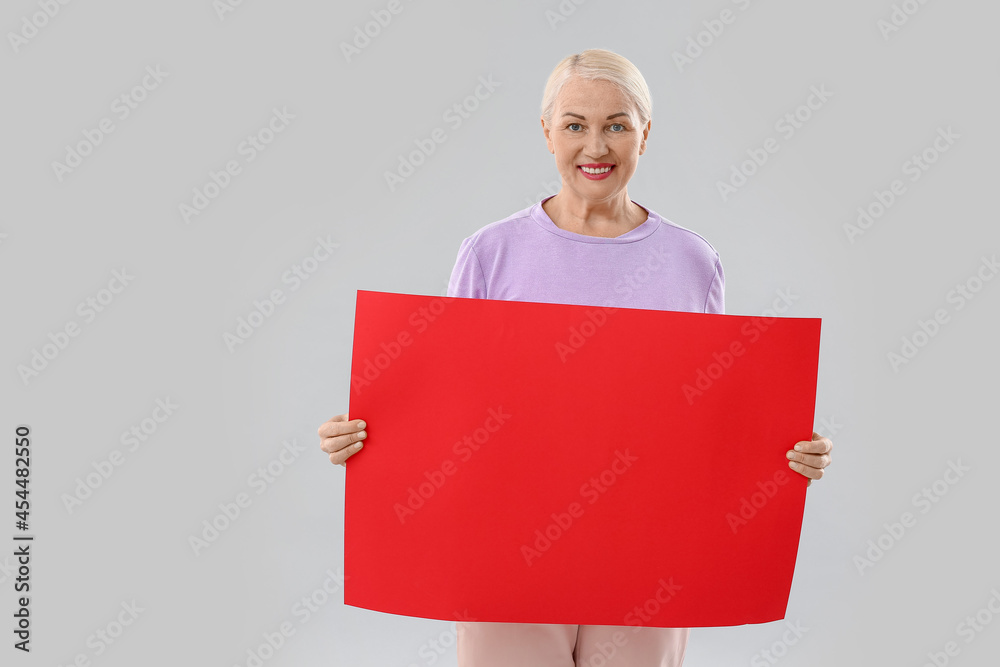 Mature woman with blank poster on light background