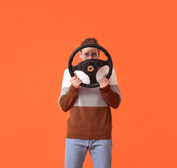 Young man with steering wheel on color background