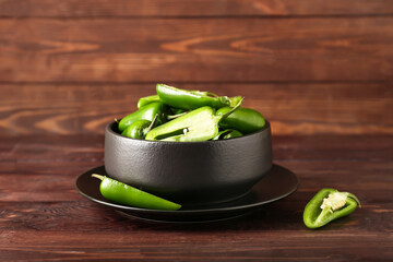 Bowl with cut green jalapeno peppers on wooden background