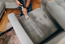 Handsome young man cleaning furniture. Process of deep furniture cleaning, removing dirt from sofa. Washing concept.
