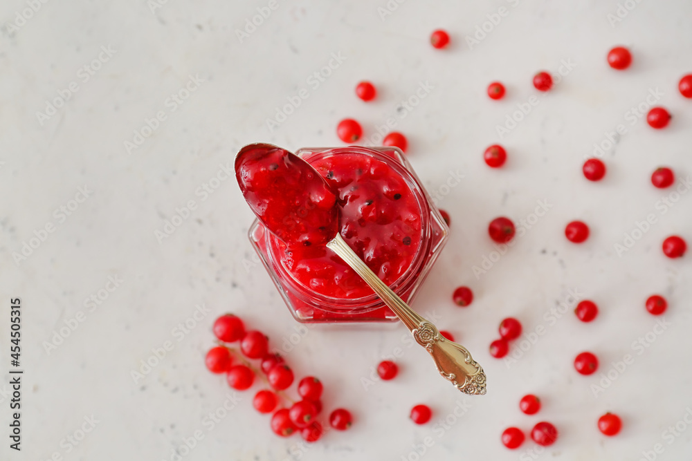 Jar of red currant jam and berries on light background