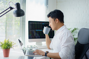 Poster - Coffee break. Young businessman or trader is drinking a coffee while looking at monitor screen with financial data in his modern office