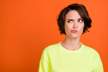 Poster - Photo of young doubtful curious minded woman look empty space wear sweatshirt isolated on orange color background