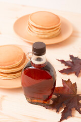 Wall Mural - Beautiful Canadian maple syrup in a bottle on a light wooden background. Pancakes with syrup or honey.
