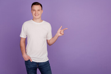 Wall Mural - Portrait of confident man direct forefingers empty space hand pocket on violet background