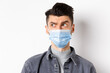 Pandemic lifestyle, healthcare and medicine concept. Confused guy in face mask look left at logo and frowning skeptical, standing on white background