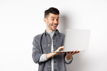 Man watching funny video on laptop, laughing at computer screen and smiling joyful, standing on white background