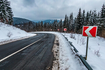 Snowed guide road sign of turn on a winter curved road through the mountains. Sharp turn on mountain road. Asphalt road at rocky mountains.