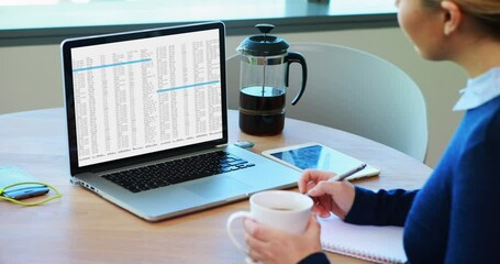 Poster - Caucasian woman sitting at desk processing on laptop and making notes