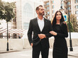 © halayalex - Beautiful fashion woman and her handsome elegant boyfriend in suit. Sexy brunette model in black evening dress. Fashionable couple posing in the street in Europe. Brutal man and his female outdoors