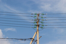 Concrete Electrical Power Line Utility Pole With Green Glass Insulators And Six Parallel Connected Overhead Wires Against Blue Sky Background.