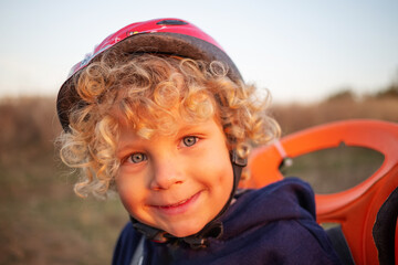 Wall Mural - White curly boy in a helmet in a bicycle seat