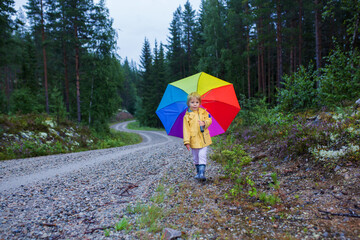 Poster - Cute toddler child with colorful umbrella, playing in the forest on a rainy day