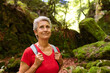 © Alberto - Happy elderly woman with gray hair and backpack contemplating the forest landscape during a hiking route through the mountains.