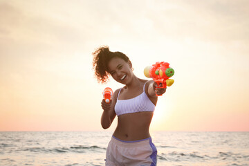 Canvas Print - African American woman with water guns having fun on beach at sunset