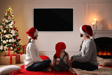 Family Watching TV In Room Decorated For Christmas