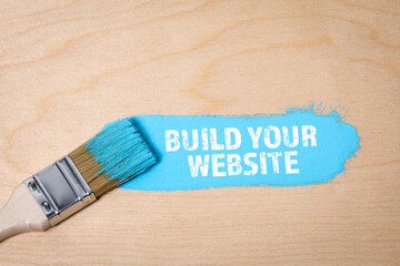 Wall Mural -  Build Your Website. Blue color and a brush on a wooden plate background