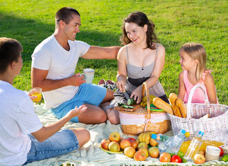 Wall Mural - Happy parents with two kids having picnic together on green meadow in park. High quality photo