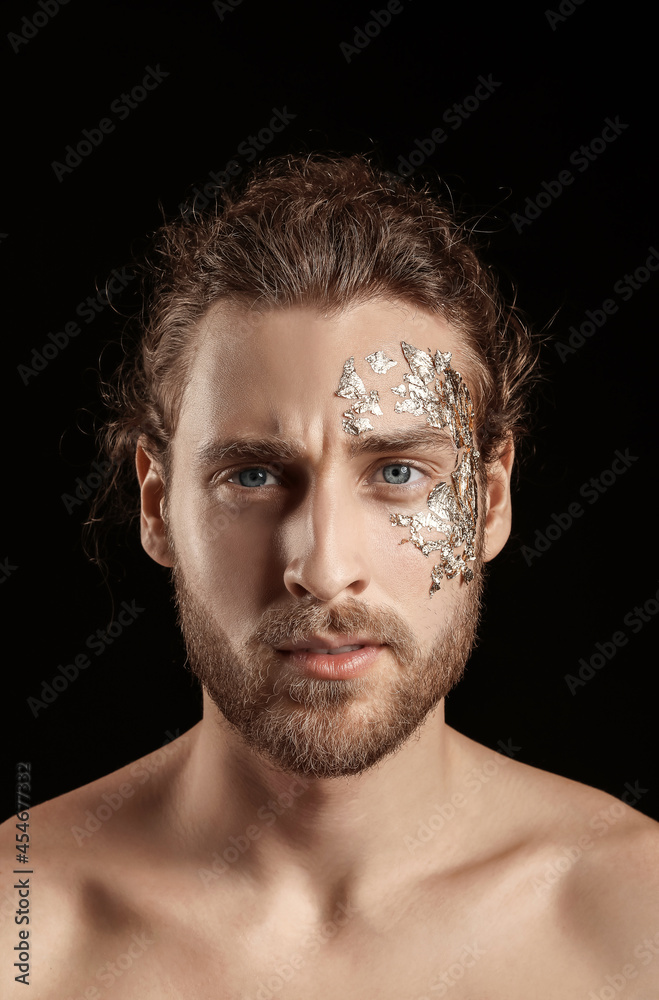 Handsome young man with golden foil on face against black background