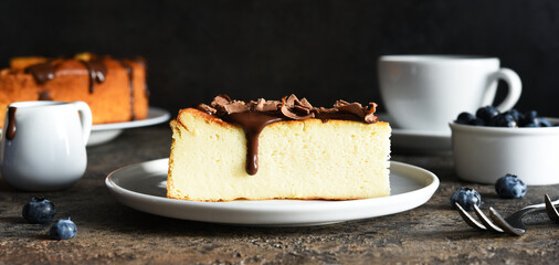 Wall Mural - Cheesecake new york. Slice cheesecake with chocolate sauce and a cup of coffee on a dark concrete background.