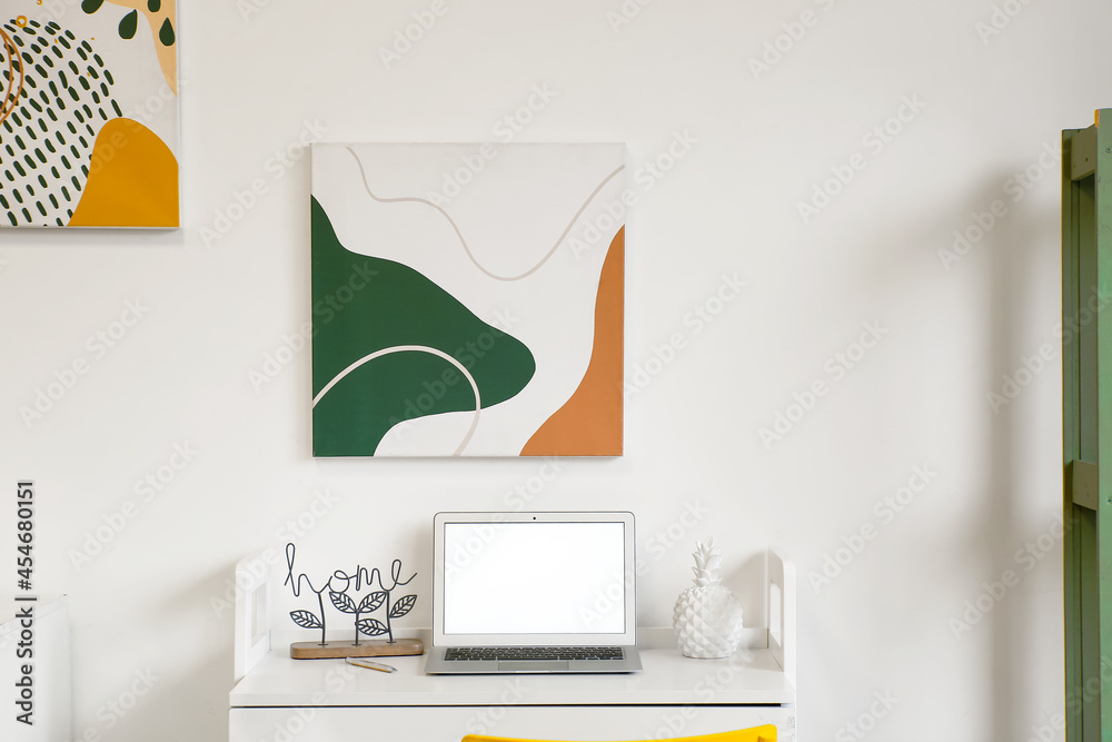 Modern workplace with laptop near light wall