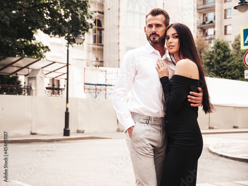Beautiful fashion woman and her handsome elegant boyfriend in suit. Sexy brunette model in black evening dress. Fashionable couple posing in the street in Europe. Brutal man and his female outdoors