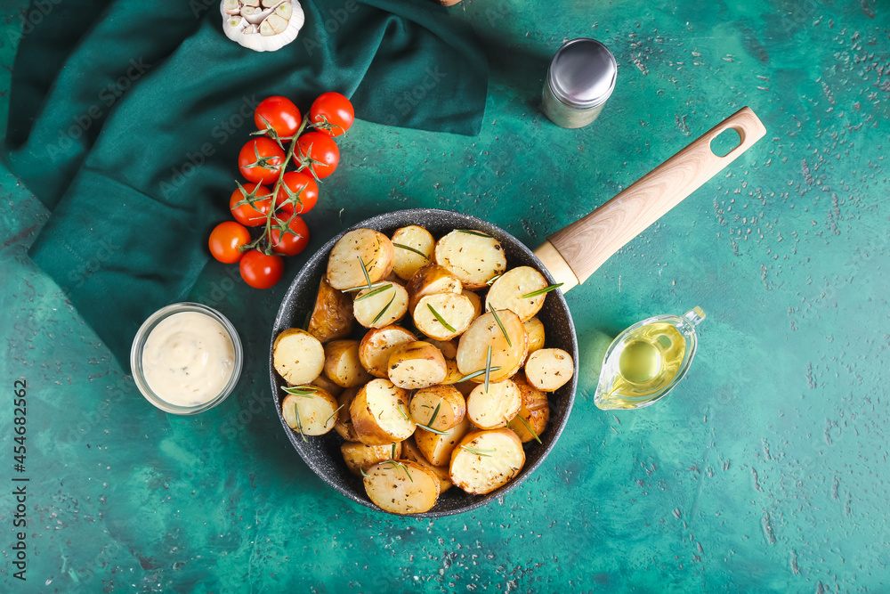 Frying pan with baked potatoes and rosemary on color background