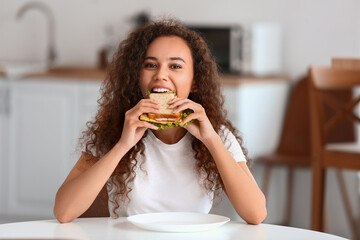 Sticker - Young African-American woman eating tasty sandwich in kitchen