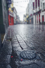 Rain Drops On Stone Pavement In Focus. Empty Small Street With Shops Of Old Town Out Of Focus. Dark And Muted Colors, Autumn And Fall Season Concept. Galway City, Ireland. City Scene