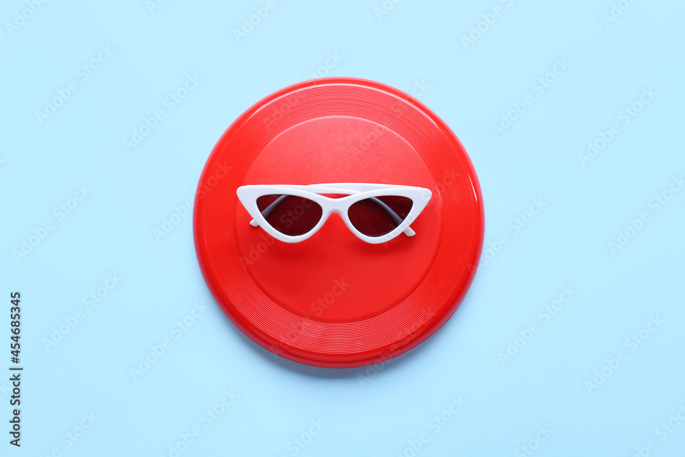 Frisbee disk and sunglasses on color background