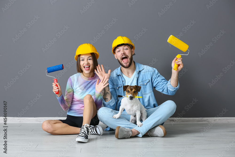 Young couple with painter's tools and cute dog near grey wall