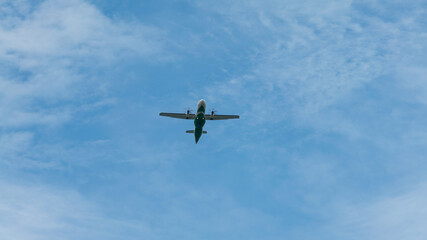 Wall Mural - View of propeller plane flying low with blue sky and clouds at background.