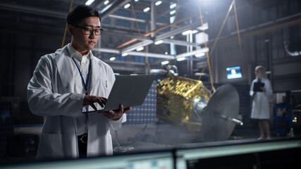 Wall Mural - Industrial Engineer Working on Artificial Satellite Construction. Aerospace Agency: Asian Scientist Using Laptop Computer to Develop Spacecraft for Space Exploration and Data Communication.