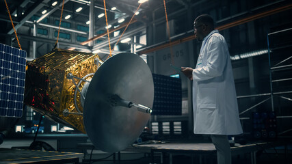 Wall Mural - Industrial Engineer Working on Artificial Satellite Construction. Aerospace Agency: African American Scientist Using Tablet Computer to Develop Spacecraft for Space Exploration and Data Communication.