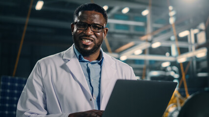 Wall Mural - Industrial Engineer Working on Artificial Satellite Construction and Smiling on Camera. Aerospace Agency: African American Scientist Using Laptop Computer to Develop Spacecraft for Space Exploration.