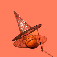 Halloween concept made of striking black with golden printed decorative witch hat and lovely orange pumpkin. Sunny shadows. Terracotta creative background.