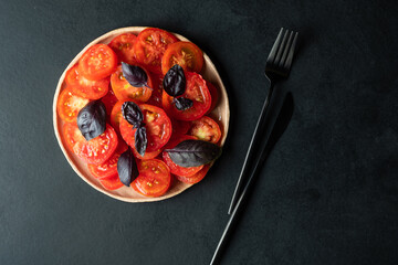 Wall Mural - Tomatoes chopped with circles, with a basil on a round plate on a dark background. 